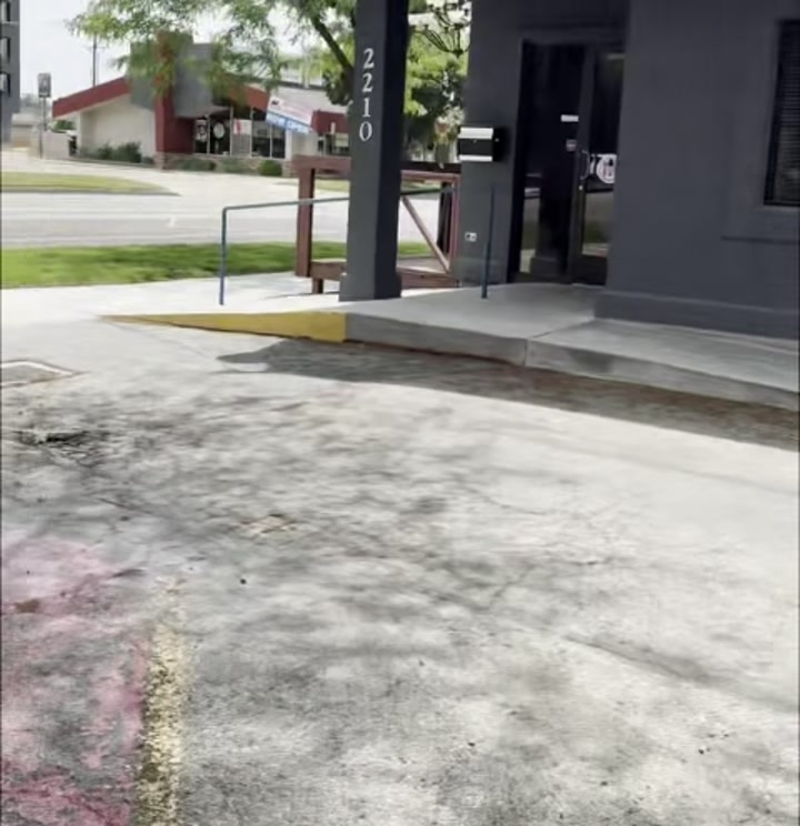 Sidewalk view approaching the building entrance at 2210 W. Main Street, address marker visible above the front doors